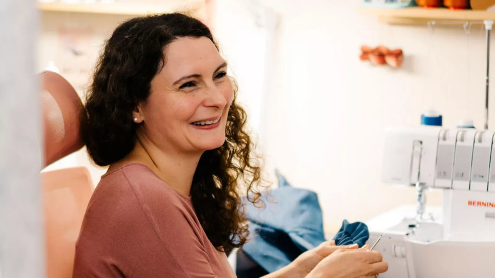 Eine Frau sitzt vor einer Nähmaschine mit einer Nadel in der Hand