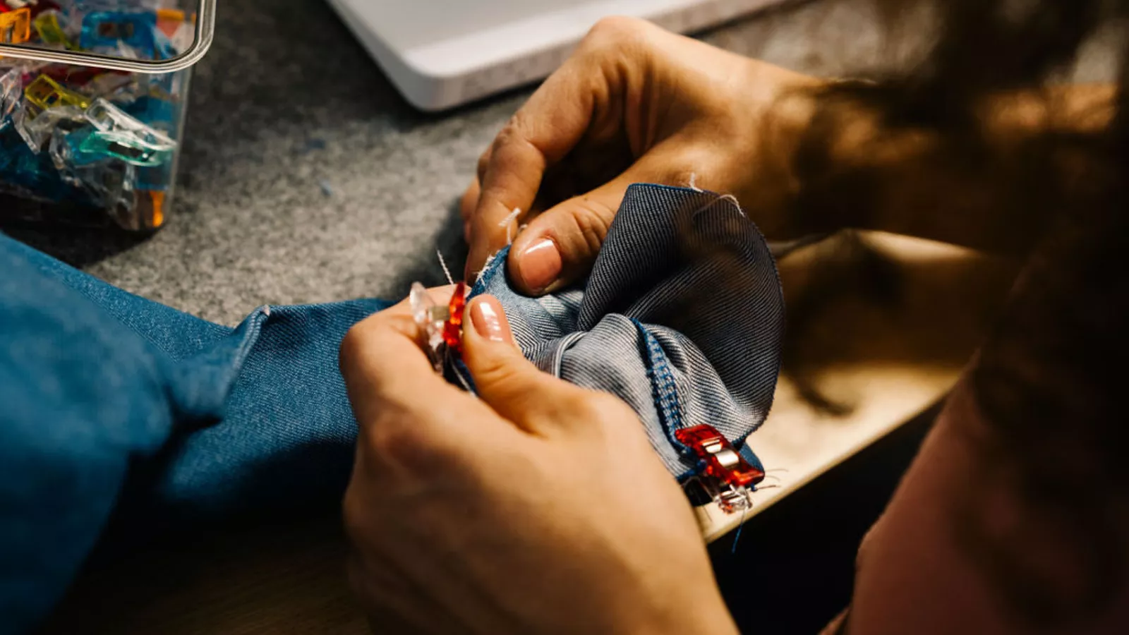 Ein Jeansstoff wird versäubert, eine Frau zieht den Stoff an der Kante und er ist mit Klammern fixiert
